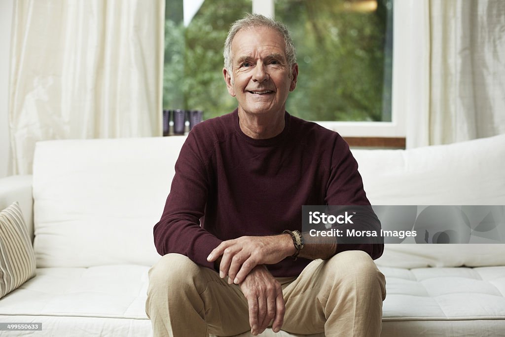 Thoughtful senior man looking away on sofa Thoughtful senior man looking away while sitting on sofa at home Sitting Stock Photo