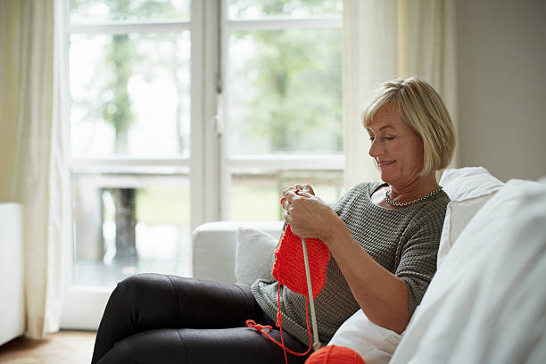 senior woman knitting on sofa - tricoté photos et images de collection