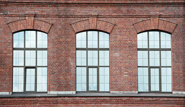 Three window on a red old brick wall