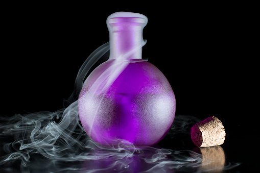 Purple bottle isolated in black background with smoke overflowing.
