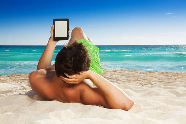 man リラックスできるビーチで読書年度版を電子書籍で - reading beach e reader men ストックフォトと画像