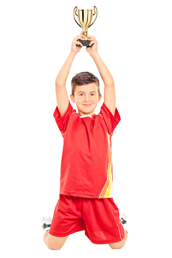 Joyful little boy holding a trophy above his head isolated on white background
