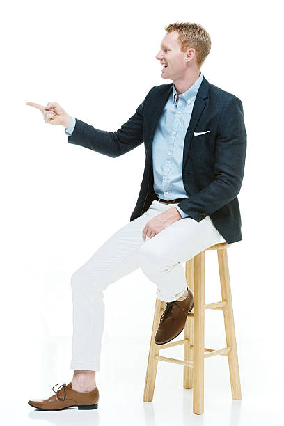 istock Fashionable man sitting on stool & pointing 499558591