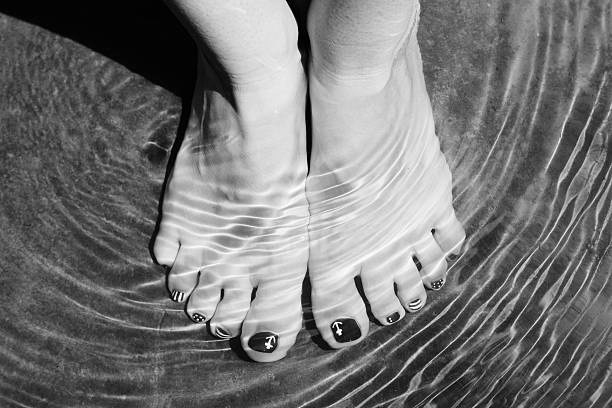 Female feet with pedicure in transparent sea water. Beautiful water surface. Enjoying nature, cooling in hot weather. Black and white photo