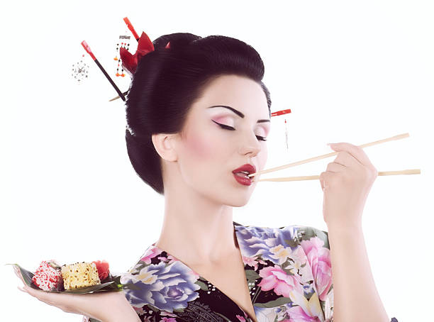 Young woman in Japanese kimono with chopsticks and sushi roll stock photo