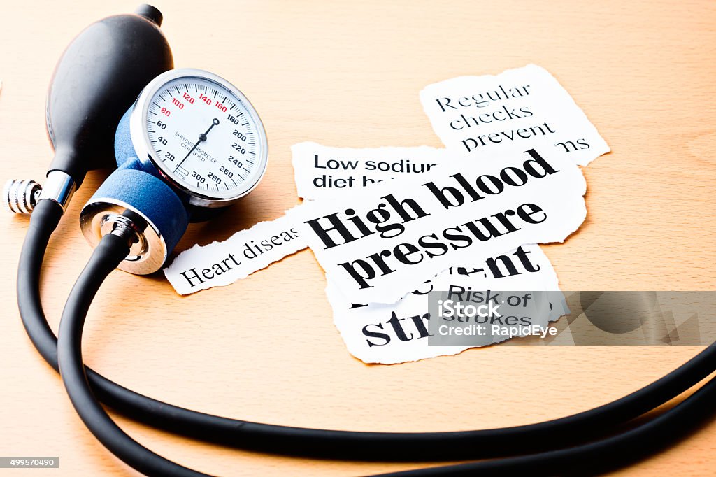 Headlines on hypertension with blood pressure meter Headlines on high blood pressure, heart disease, and the risk of strokes on a wooden desk next to a blood-pressure gauge. Heart Disease Stock Photo