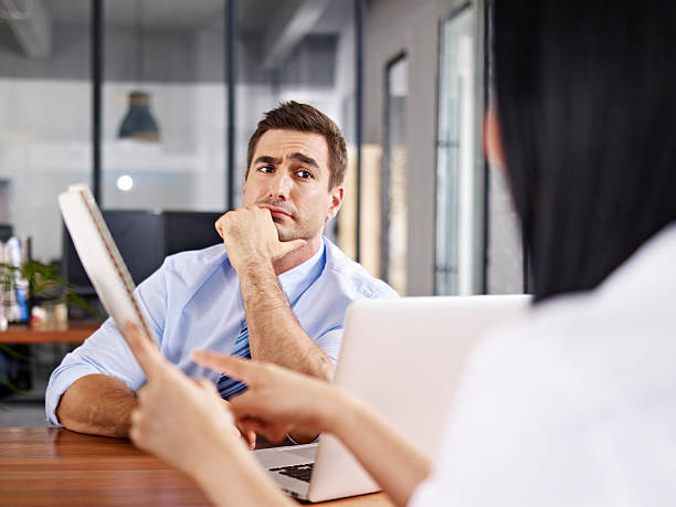 skeptical interviewer looking at interviewee a caucasian male interviewer looking skeptical while listening to an asian female interviewee. persuasion stock pictures, royalty-free photos & images