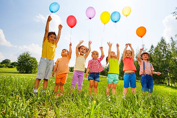 glückliche kinder mit luftballons und arme hoch in den himmel - friendship park flower outdoors stock-fotos und bilder