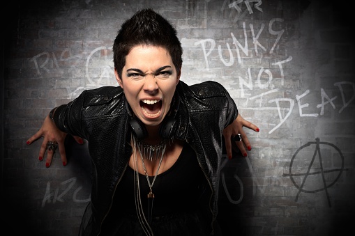 Punk girl leaning against wall and shouting into camera aggressively.
