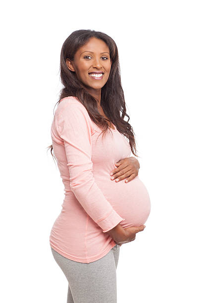 Smiling pregnant woman. Studio shot  of 8 months pregnant woman stroking her belly and looking over the camera. Cut out image. with copy space. 8 months pregnant stock pictures, royalty-free photos & images