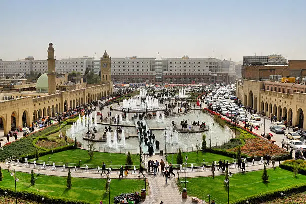 Erbil / Hewler / Arbil / Irbil, Kurdistan, Iraq: main square, Shar Park, with crowds enjoying the pleasantly cool area created by the fountains - arcades on both sides and Nishtiman mall in front - Mosque and Erbil Clocktower on the left - dense traffic on Kirkuk avenue on the right - seen from the Erbil citadel - photo by M.Torres