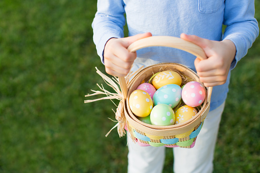 easter and spring concept, boy holding basket full of colorful eggs standing on the grass