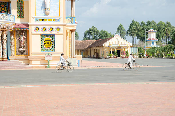 zwei alte mann reiten fahrrad in cao dai-tempel - caodaism stock-fotos und bilder