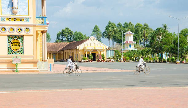 zwei alte mann reiten fahrrad in cao dai-tempel - caodaism stock-fotos und bilder