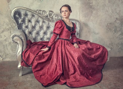 Beautiful young woman in red medieval dress on the sofa