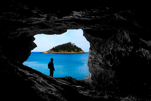 alone traveler look a beautiful island from inside a cave, backlight silhouette, discover new places to travel, people travelling