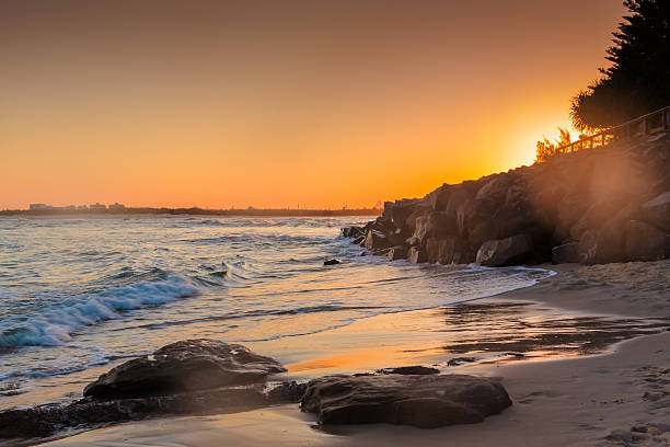 The sun sets behind the rocks and the broadwalk in the beautiful beach town of Caloundra, Queensland, Australia.