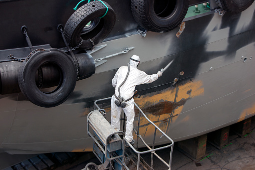man spray painting hood of ship grey in dock