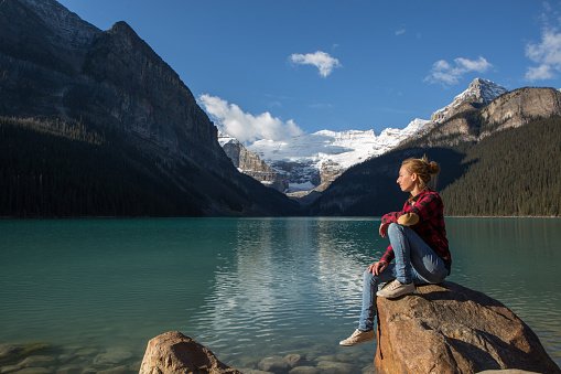Young woman sitting on a rock by the lake relaxing and enjoying the spectacular landscape.