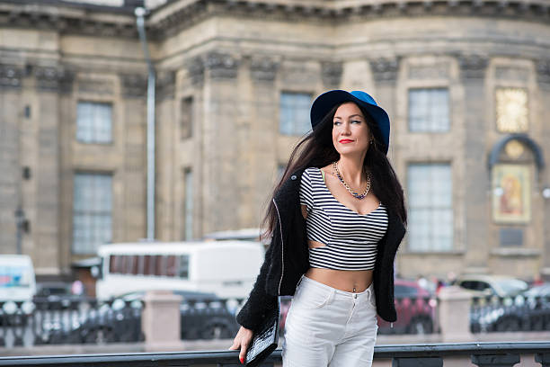 Half length portrait of beautiful young woman with a gentle smile wearing stylish hat while posing on the bridge in urban setting,