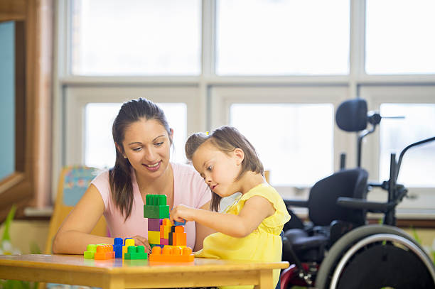 Building a Toy Tower on a Table A little girl with cerebral palsy is trying to stack toy blocks with the help of her caregiver. teacher classroom child education stock pictures, royalty-free photos & images