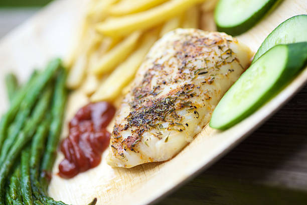 baked blackened wild caught cod fillets organic catsup, potato fries, cucumbers and fresh basted asparagus on banana leaf