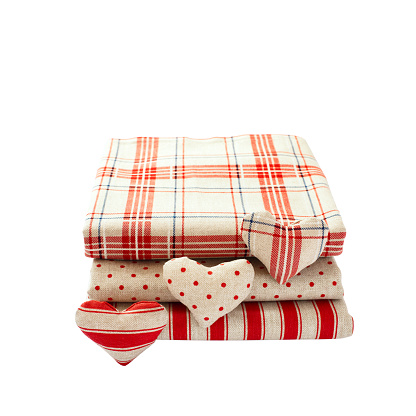linen fabric with red polka dots, plaid and stripes for needlework stacked in pile isolated. Heart made of cloth.