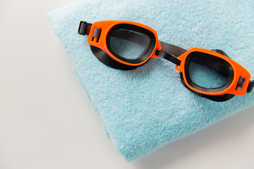 sport, fitness, water sports and objects concept - close up of swimming goggles and towel