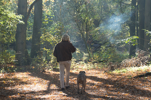 Men smoking a cigarette in the forest while he is walking his dog