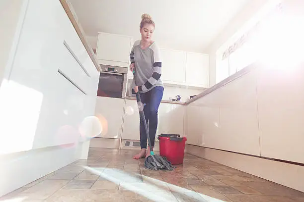 One woman mopping the floor in her kitchen.