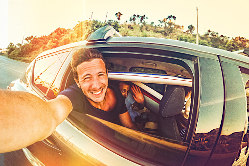 Group of surfers making a selfie during a road trip, while driving in a over packed car, stuffed with surfboards