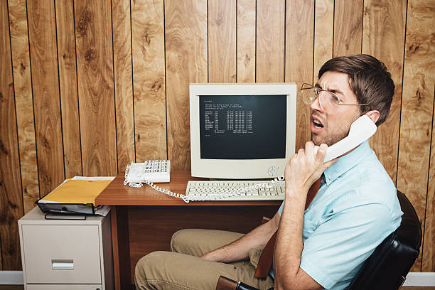 Confused and Bored Office Worker A man and office in 1980's - 1990's style, complete with vintage computer and technology of the time, listens with a look of confusion or boredom to someone on the phone. Wood paneling on the wall in the background. Horizontal with copy space. nerd stock pictures, royalty-free photos & images
