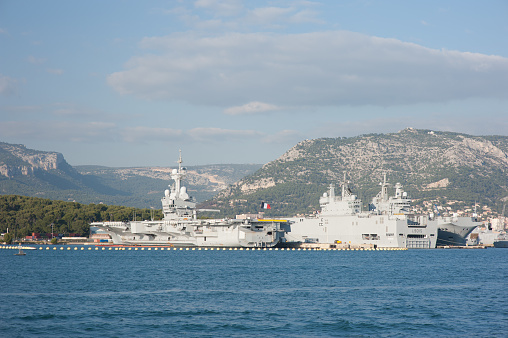 Toulon, France - October 29, 2014: The French aircraft carrier Charles de Gaulle, fying the French flag, in Toulon Harbour, where the French navy is moored when not involved in missions. To the right is the Dixmude, an amphinious assault ship, a helicopter carrier. The Charles de Gaulle is the largest naval vessel in Western Europe and weighs 38,000 tonnes. It is also the only one powered by nuclear energy.