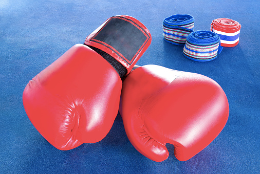 Red boxing gloves with three rolls of hand bandage on blue exercise mat.