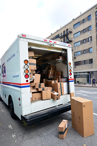 New York, USA - December 3, 2015: USPS delivery man in truck full of boxes after black friday and cyber monday sales. Sitting on the ground beside the young man is a stack of sealed boxes.