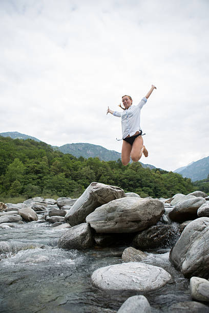 glückliche frau springen am fluss in der schweiz - arms outstretched teenage girls jumping flying stock-fotos und bilder