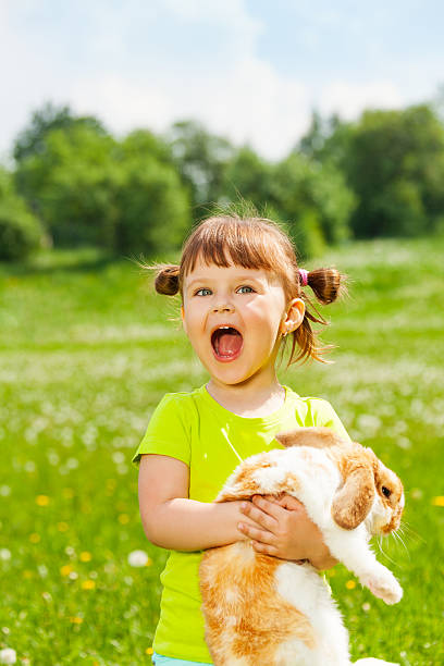 istock Excited small girl with open mouth hugging rabbit 499666443