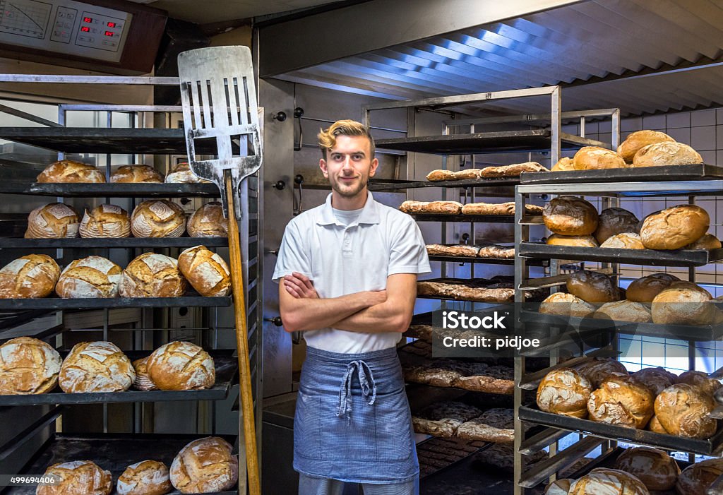 Baker in his bakery baking bread baker posing in his bakery bakehouse in the early morning between fresh baked artisan bread Baker - Occupation Stock Photo