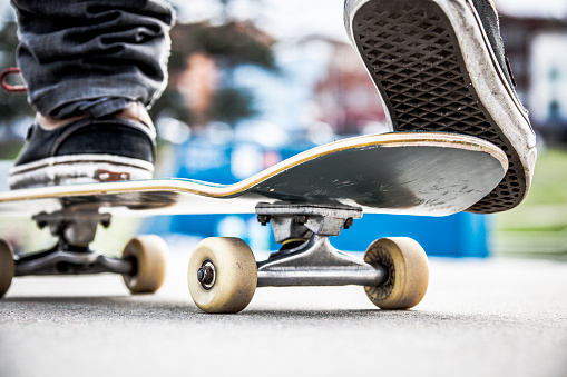Extreme close-up of the feet of a young teenage skateboarder balancing on board ready for action in local skate park.  Focus on right foot and rear of board.  Names and logos removed.