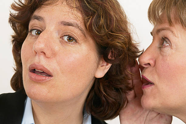 two women whisper a secret stock photo