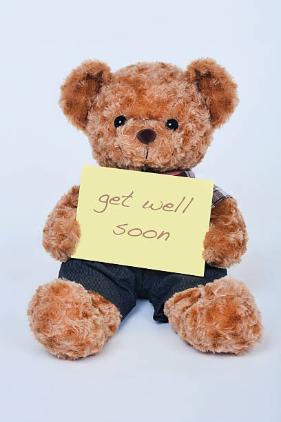 teddy bear holding a  yellow sign saying get well soon - beterschap stockfoto's en -beelden