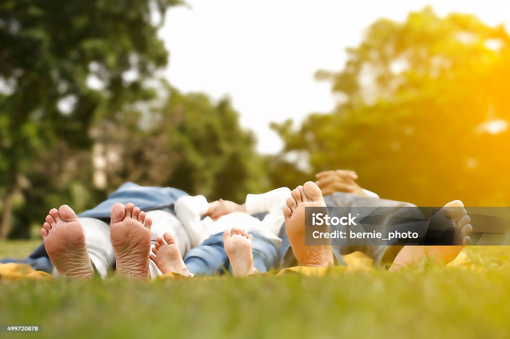 Happy family lying  outdoors together barefoot barefoot family lie on their backs in the green grass in a sunny spring park. Family Stock Photo