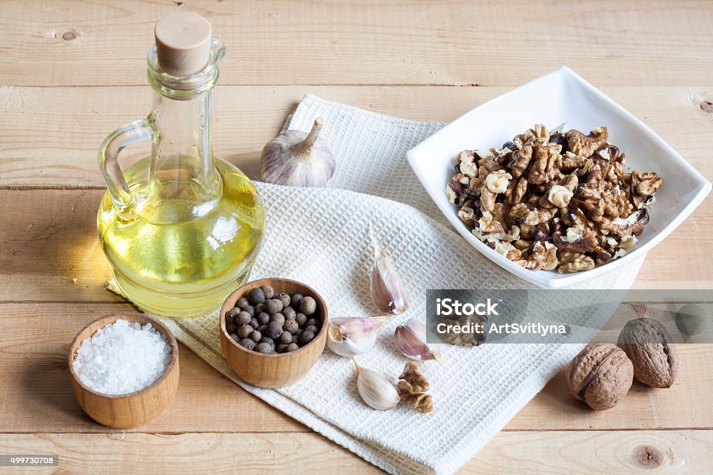 Walnuts in a white bowl, garlic, pepper salt and oil Walnuts in a white bowl, garlic, pepper salt and oil on a wooden background, wooden board and white napkin Approaching Stock Photo