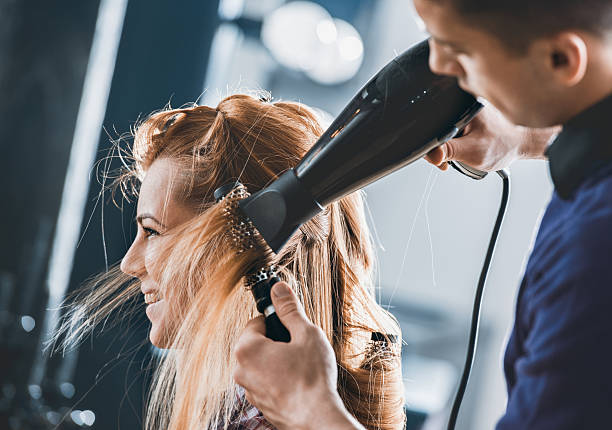Smiling woman getting her hair styled and hair salon. Young hairdresser drying customers hair with round brush at hair salon. blow drying stock pictures, royalty-free photos & images