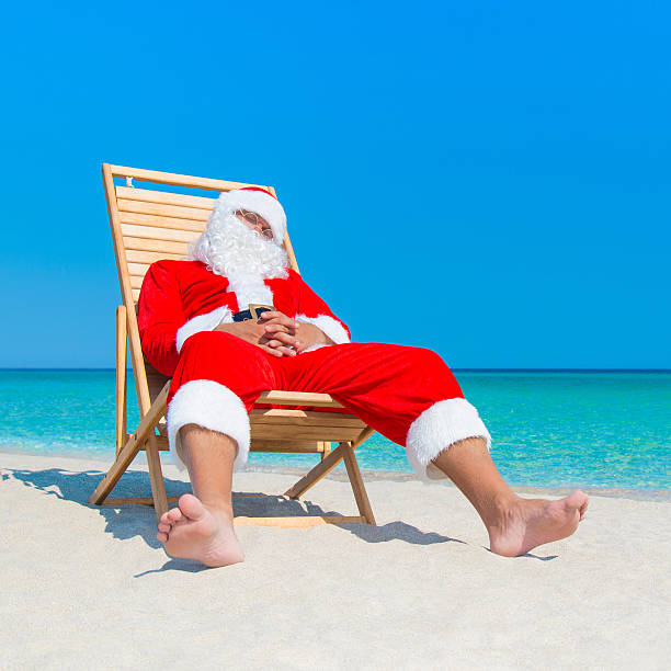 istock Christmas Santa Claus resting on deckchair at ocean sandy beach 499742196