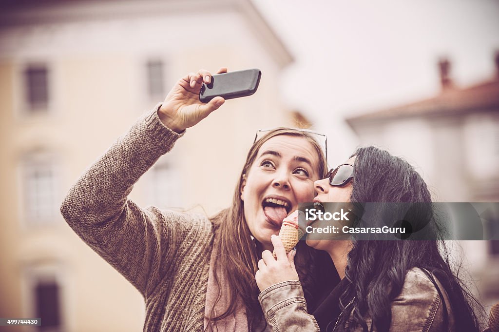 Women Taking Self Portrait while Eating Ice Cream Two female friends having fun licking one ice cream and taking self portrait 2015 Stock Photo