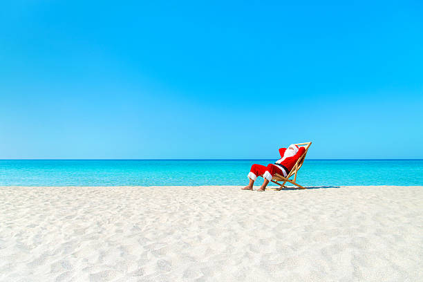 weihnachten weihnachtsmann ruhen auf den liegestuhl am meer sandstrand - weihnachtsmann stock-fotos und bilder
