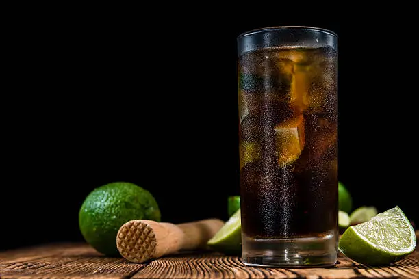 Cold Longdrink (Cuba Libre) with brown rum and fresh lime on rustic wooden background