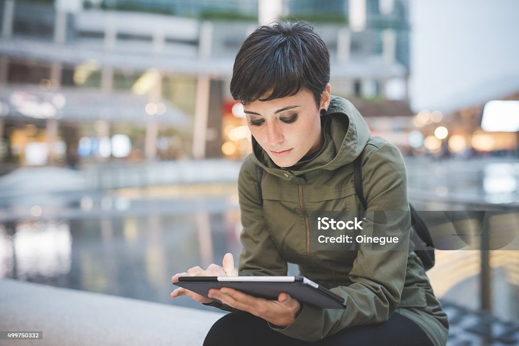 young handsome caucasian brown straight hair woman sitting in ci young handsome caucasian brown straight hair woman sitting in city dusk, holding tablet, looking downward screen, face illuminated by screen light - technology, social network, communication concept Cool Attitude Stock Photo