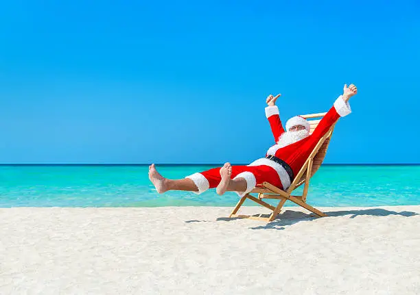 Happy Christmas Santa Claus resting on lounge chair at ocean sandy tropical beach - New Year travel vacation in hot countries concept